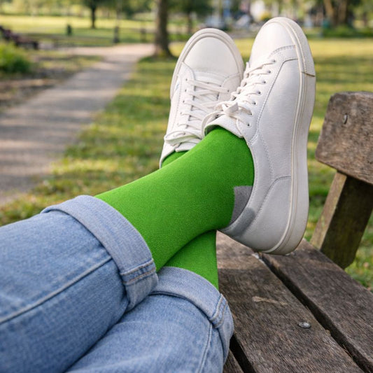 Person wearing white sneakers and green cotton socks sitting on a wooden bench in a park.