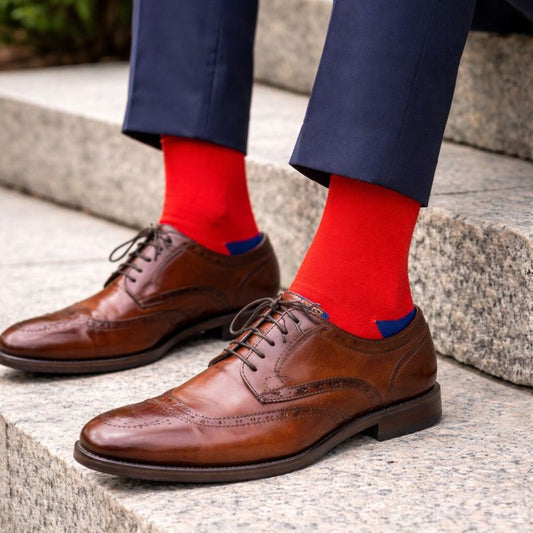 Brown dress shoes with red socks and blue accents on a stone step.