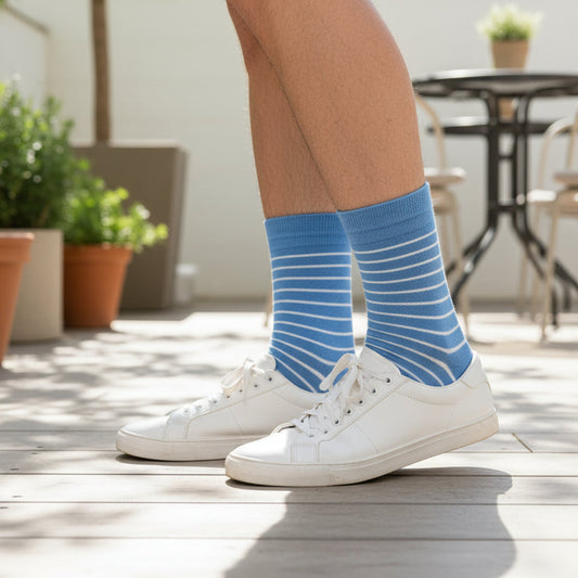 Person wearing blue striped cotton socks and white sneakers on a wooden deck.